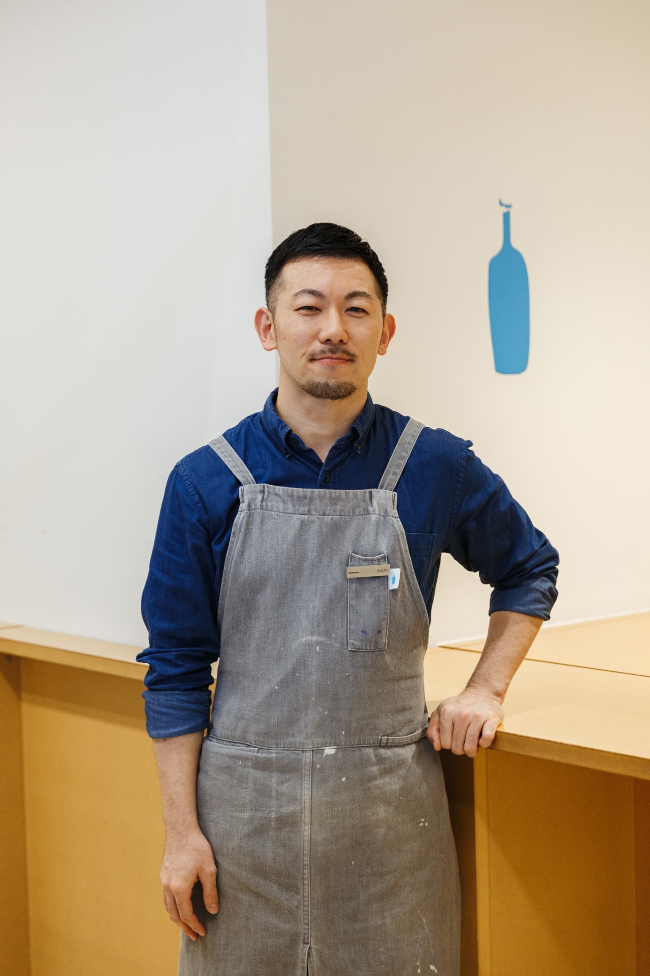 Member of staff at Shibuya's Blue Bottle Coffee outlet wearing gray apron and blue shirt