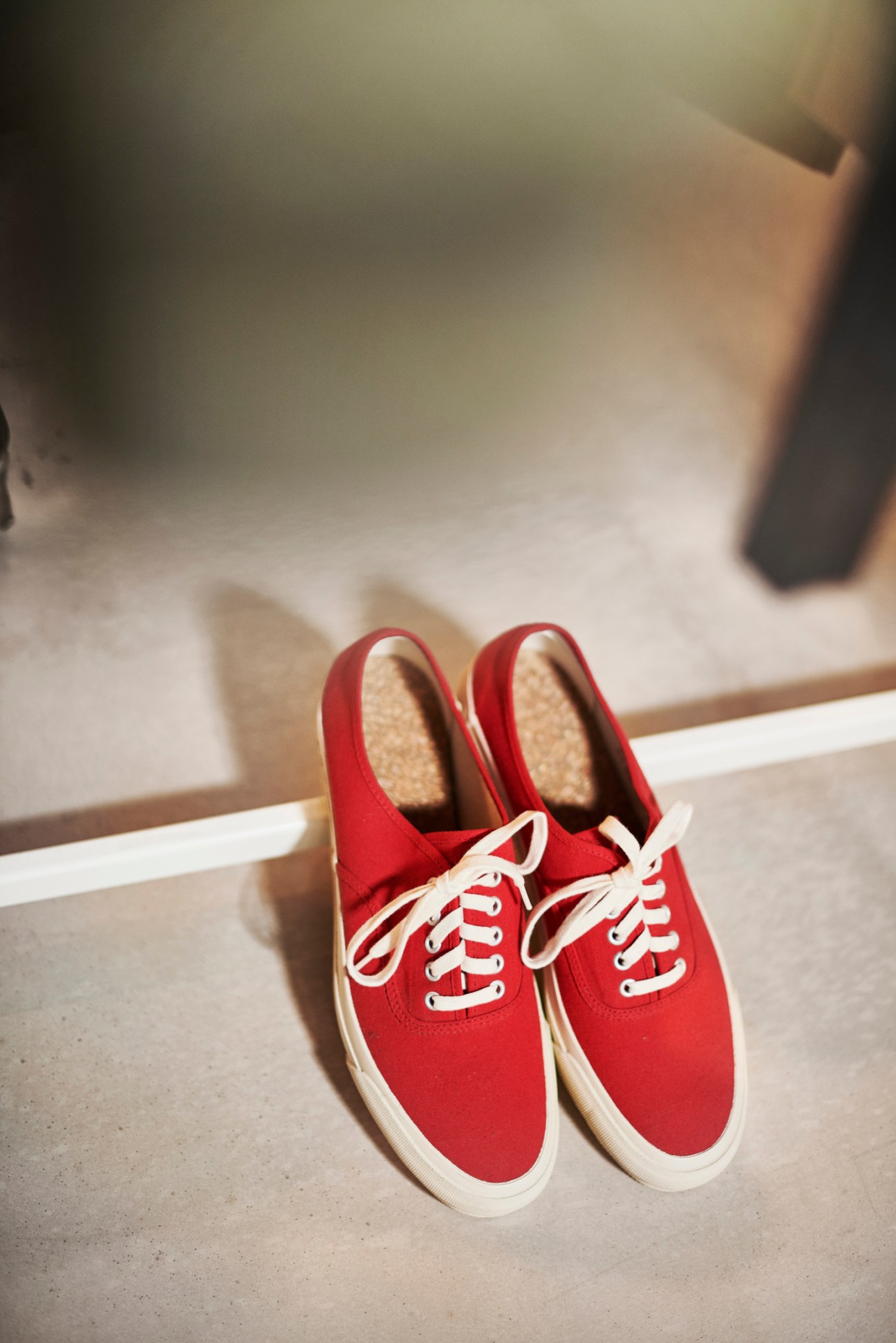 Pair of red and white canvas deck shoes by Doek with white laces displayed on concrete floor.