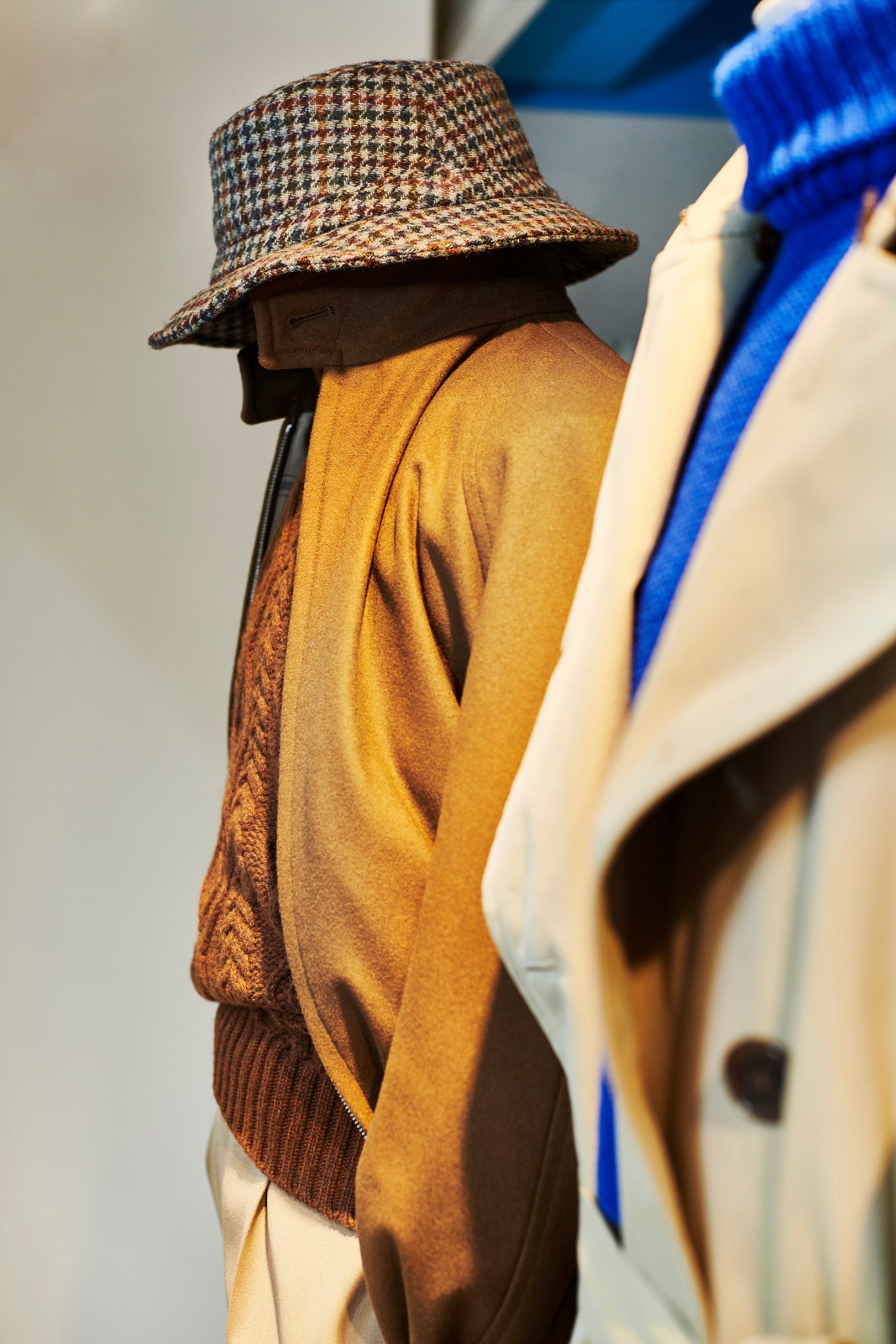 Mannequin wearing a houndstooth bucket hat by Lock and Co, mustard sweater by Inis Meáin, and brown jacket by Grenfell.