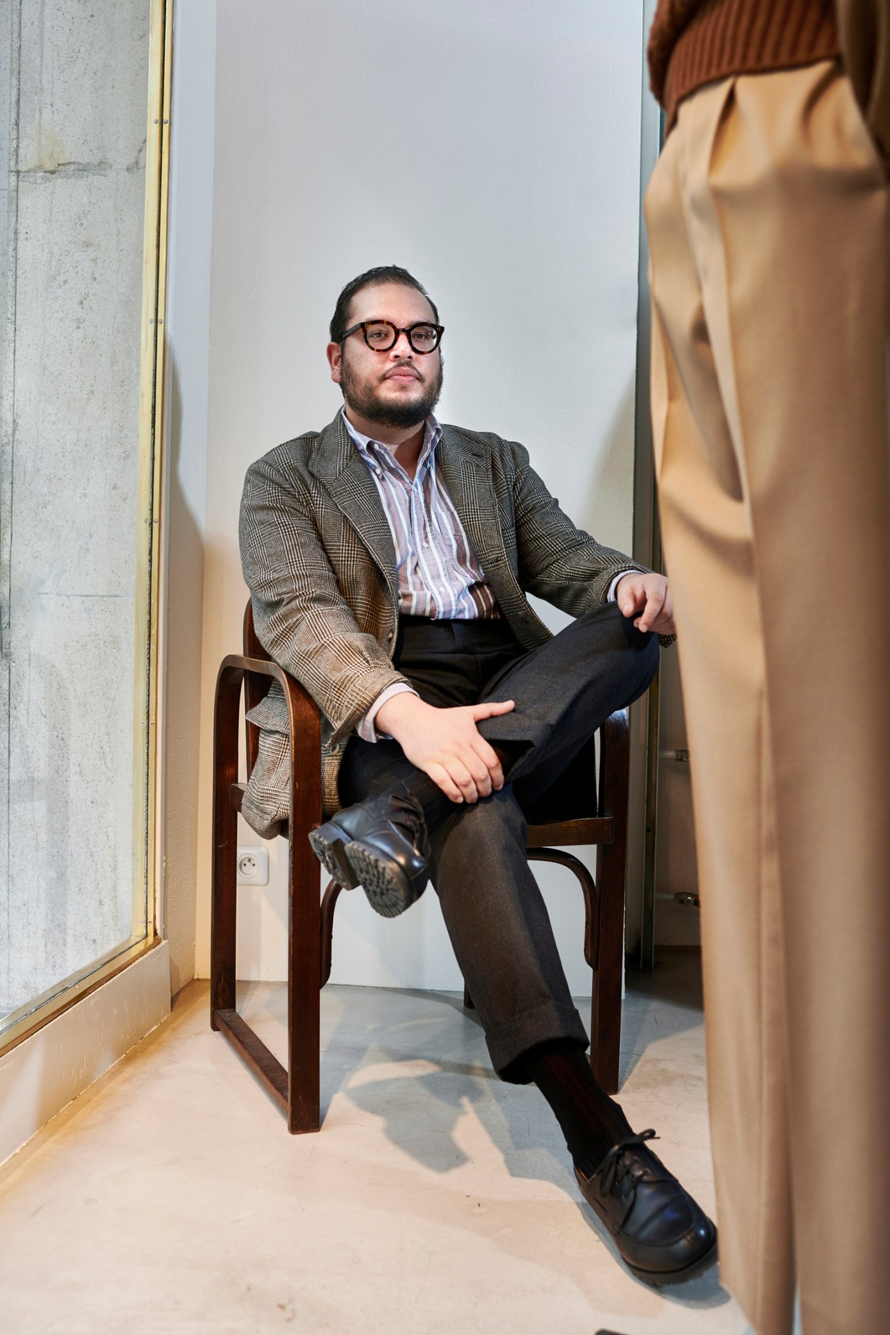 Basile Khadiry, co-owner of Beige Habilleur menswear boutique, seated in a chair wearing a patterned blazer and glasses.