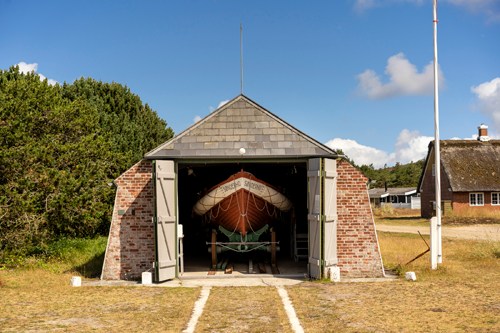 Wooden rescue boat displayed inside brick boathouse with open doors on grassy area