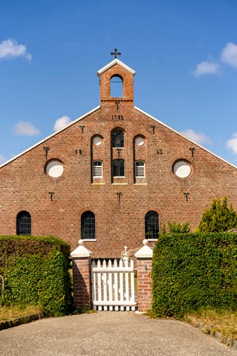 Brick church building with cross on bell tower and white gate entrance in Sønderho