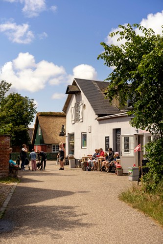 White traditional Danish house with outdoor seating area where people gather under blue sky with clouds