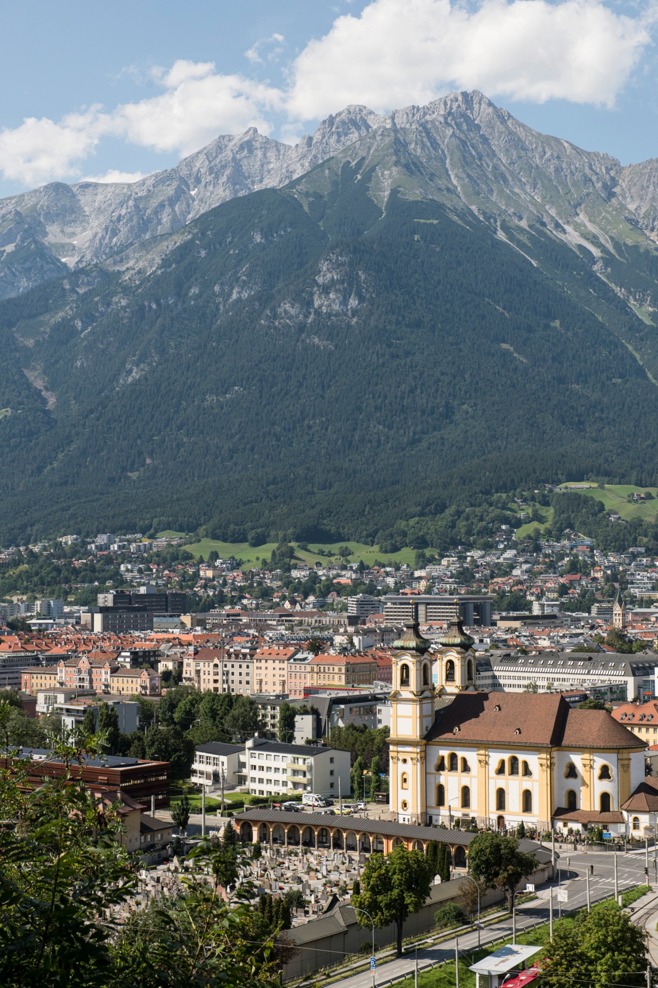Aerial view of Innsbruck showing baroque church with twin towers, residential buildings and dramatic Alpine mountains