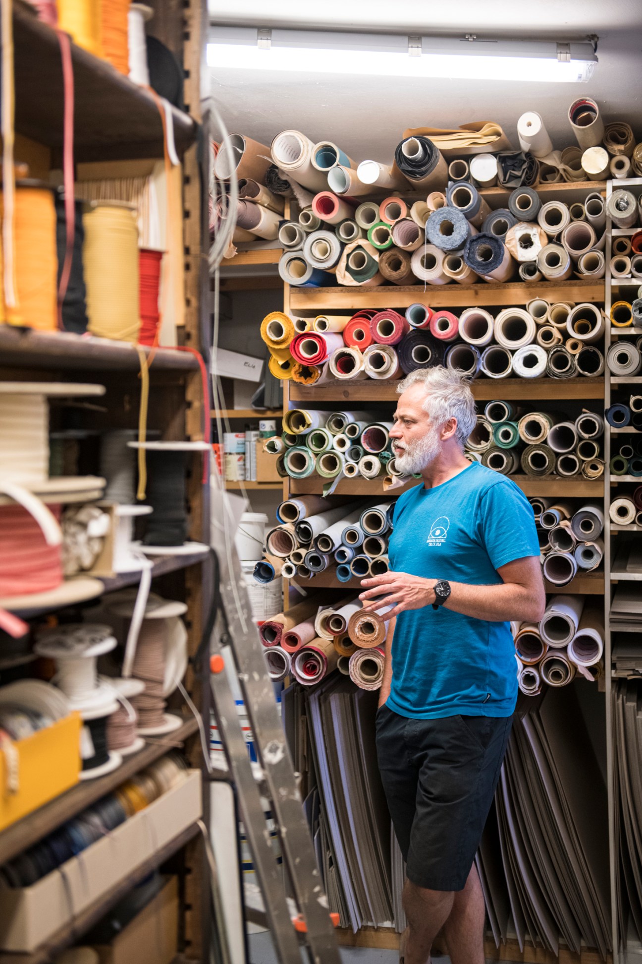 Bookbinder Bernhard Sanders standing among shelves of rolled papers and materials in his workshop