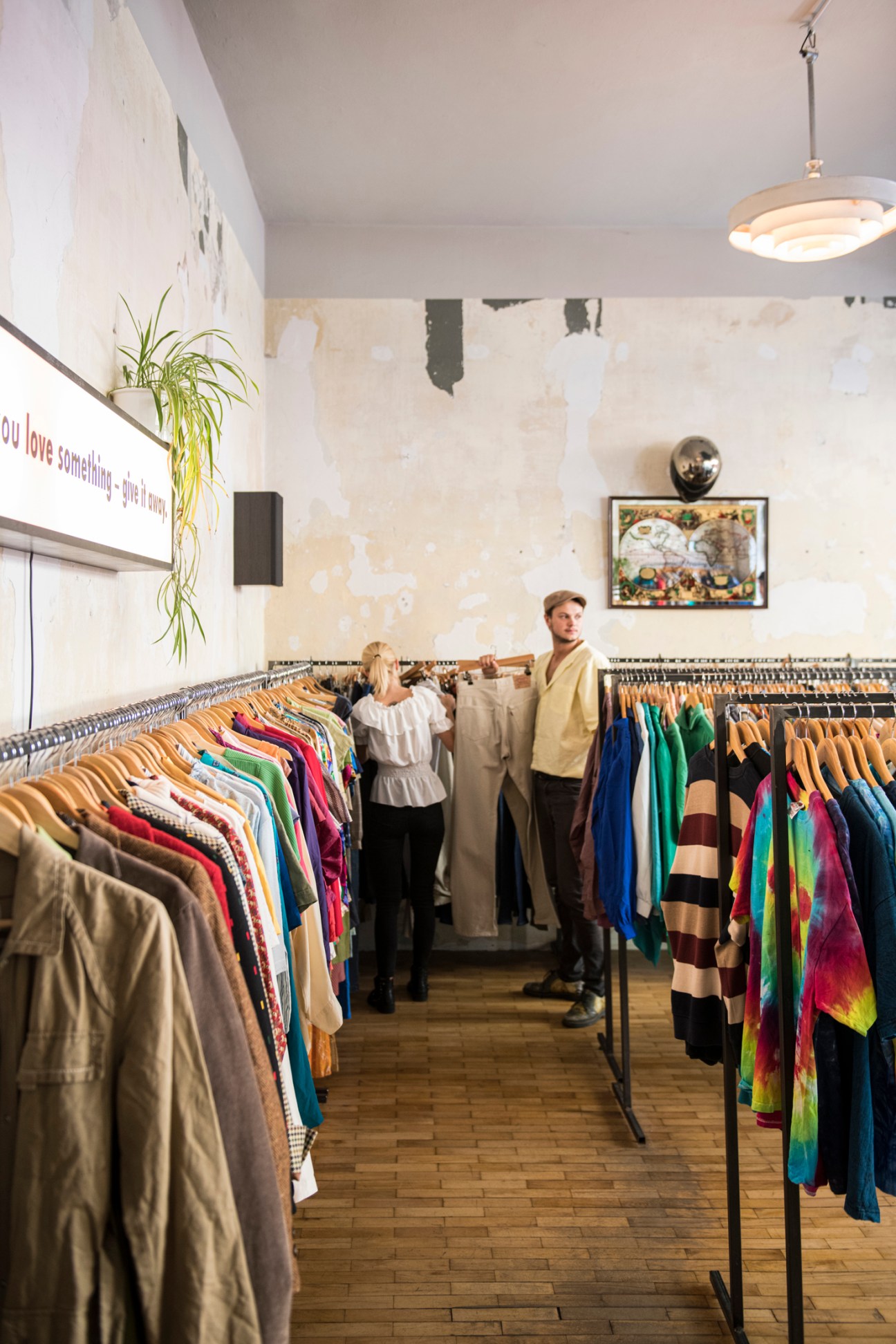 Interior of vintage clothing store with racks of colorful secondhand clothes and two people shopping