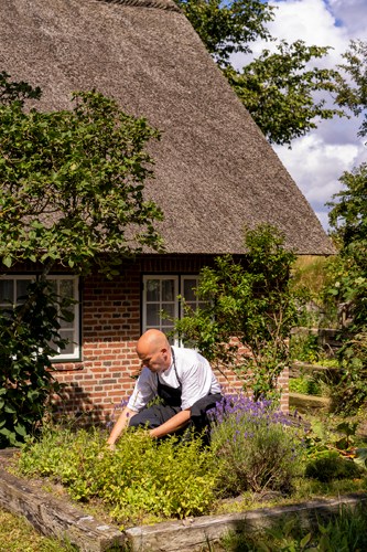 Jakob Sullestad working in a garden with traditional thatched-roof building in background