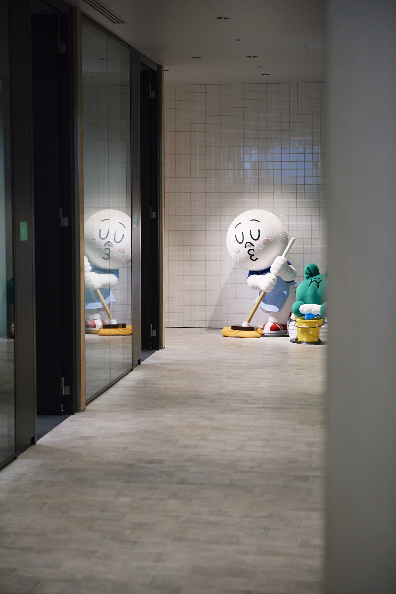 Life-sized cartoon character figures Moon and Leonard in a modern office hallway with tiled walls.
