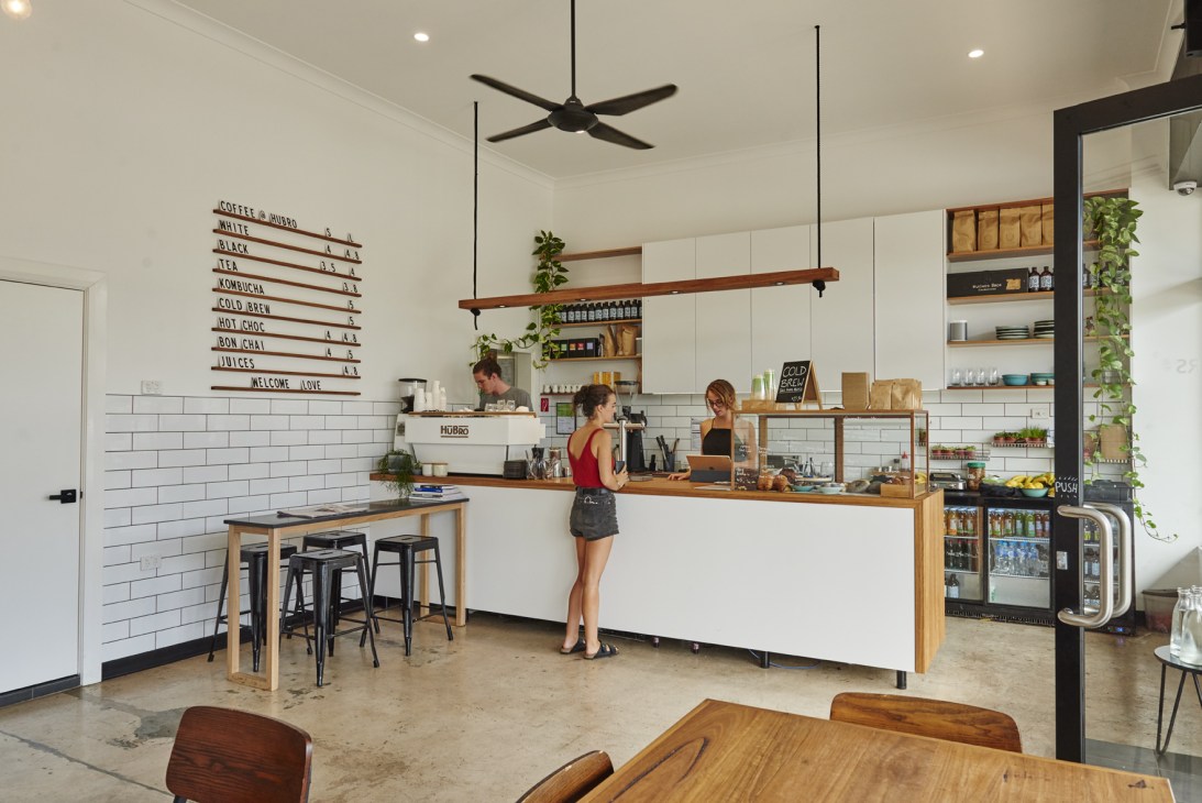 Interior of Café Hubro showing counter with white subway tiles, menu board, and customers at bar seating.