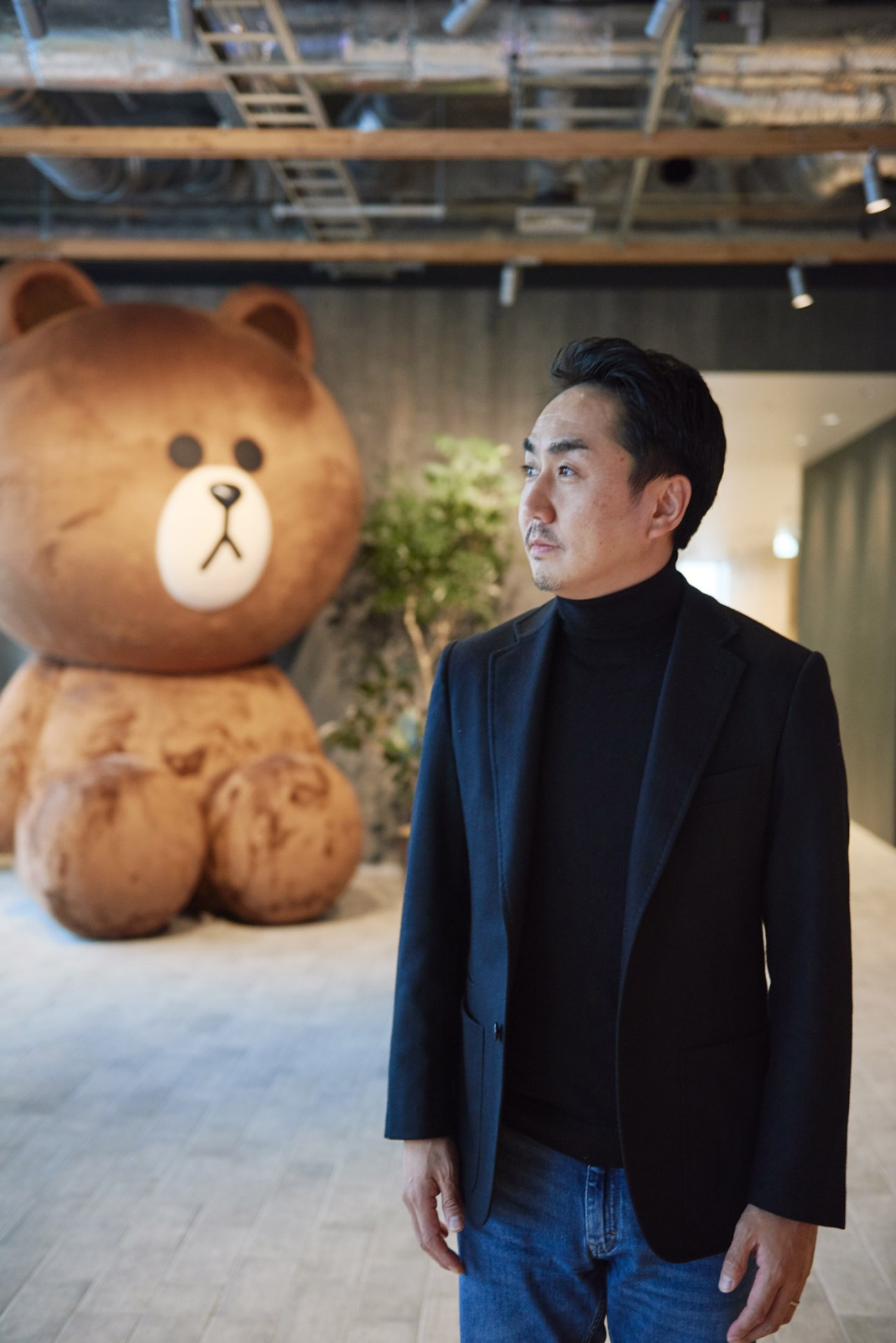 Line CEO Takeshi Idezawa stands next to a large brown cartoon bear character named Brown at Line's Tokyo office.