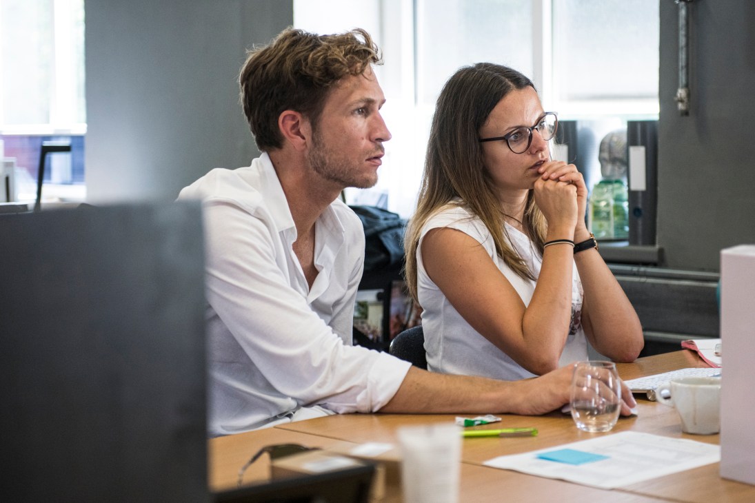 Two people sitting at a table in a modern office space looking attentively at something off-camera