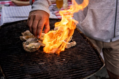 Chef grilling oysters over open flames on a barbecue grill