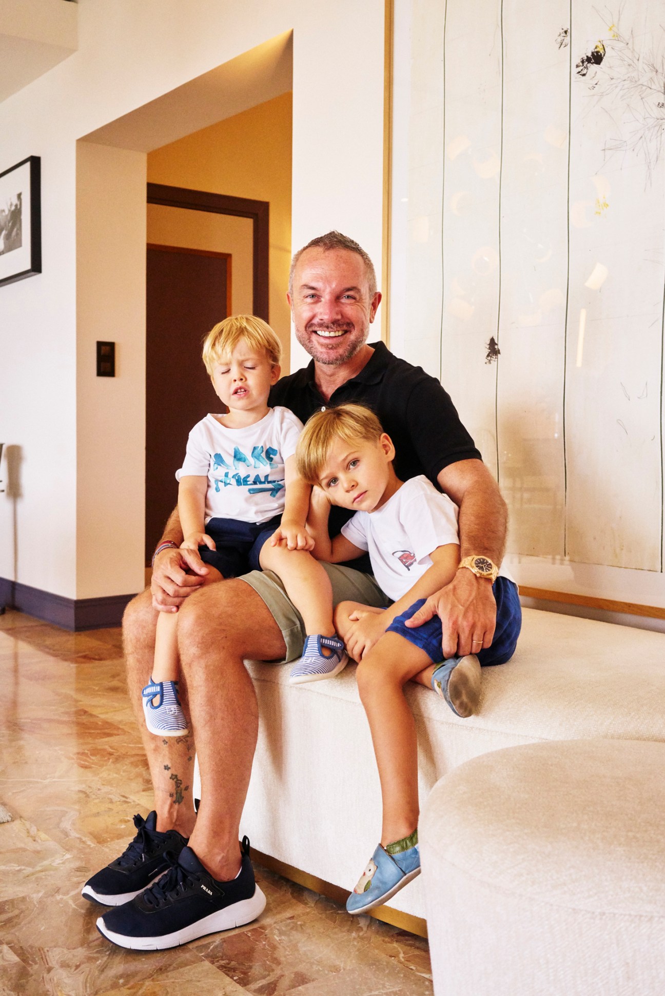 Riccardo Giraudi with his two young blonde children sitting on marble steps in modern interior