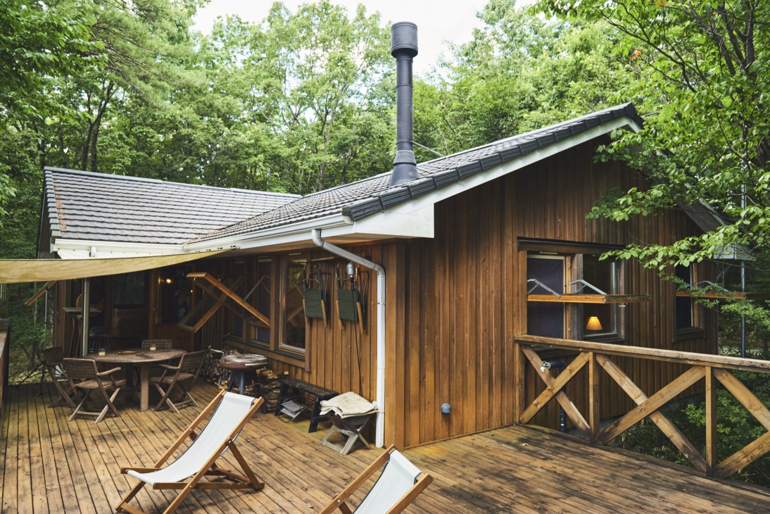 Swedish-style wooden lodge nestled among dense green trees with a wooden deck terrace featuring lounge chairs.