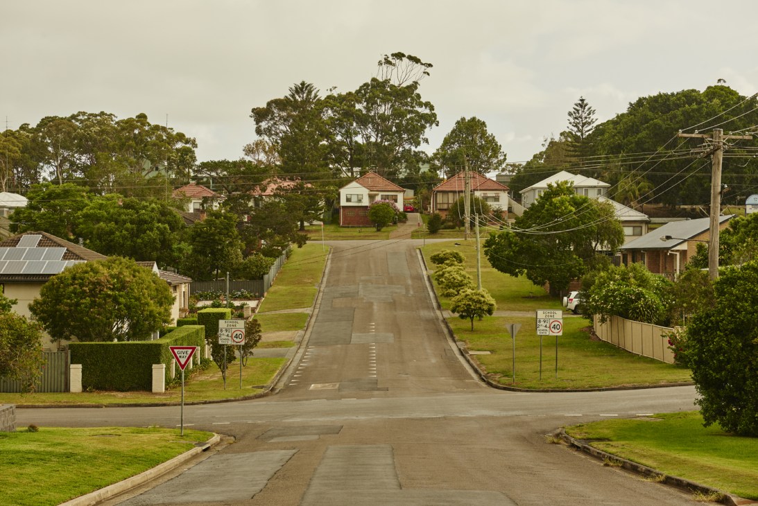 A quiet suburban street in Kahibah lined with residential homes, green lawns, and trees under an overcast sky.