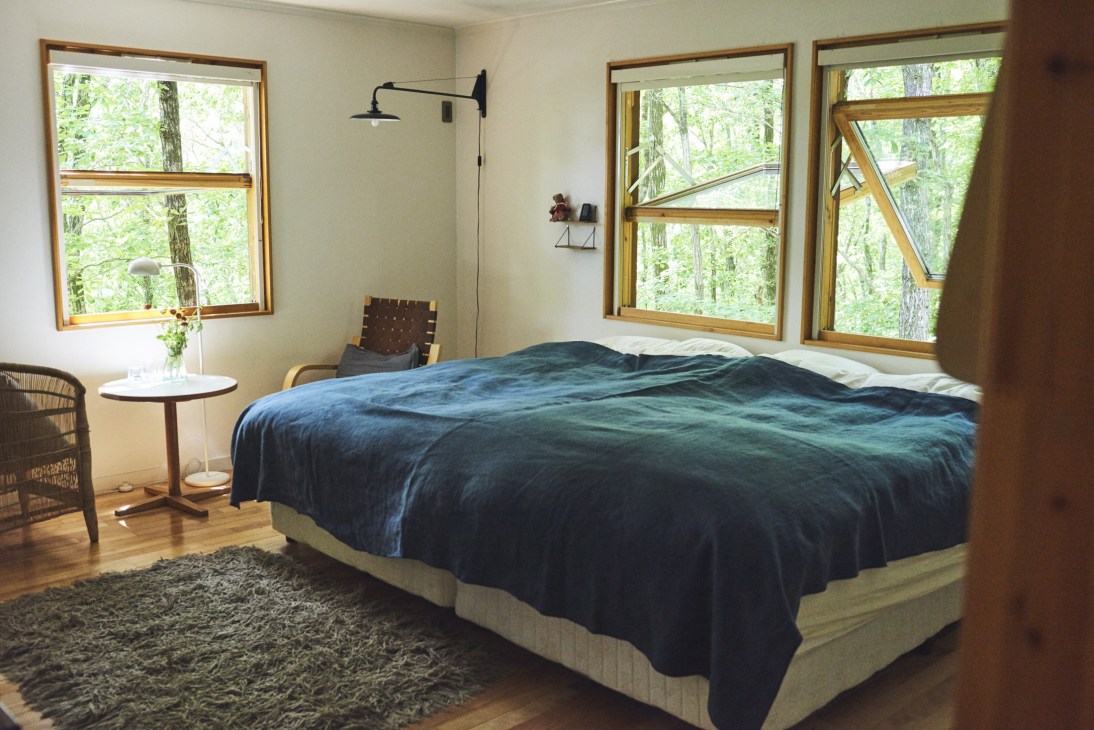 Master bedroom with large bed, wooden frames windows overlooking forest, and minimalist Scandinavian furnishings.