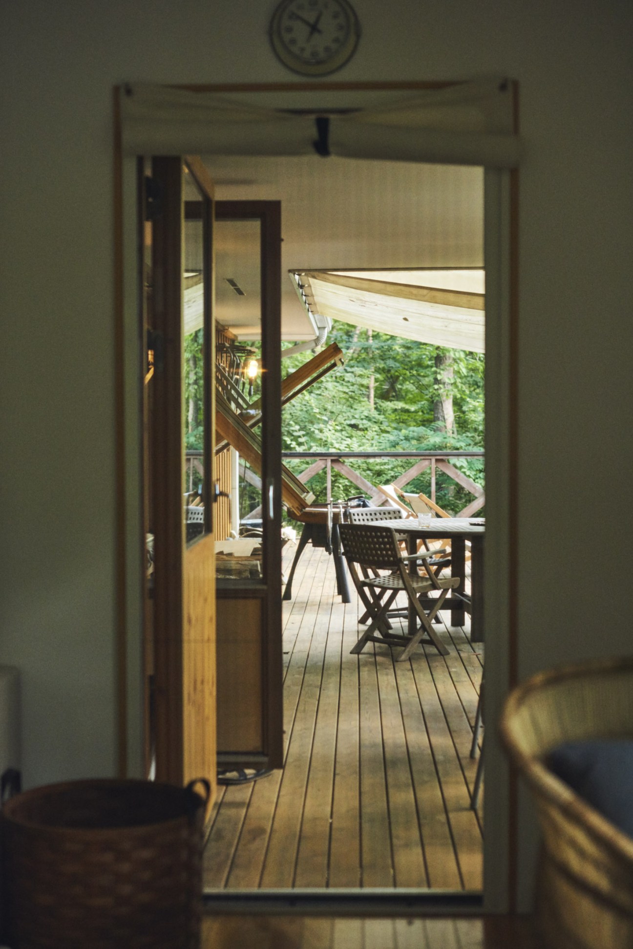 View through open glass doors from master bedroom to wooden terrace with furniture and forest beyond.