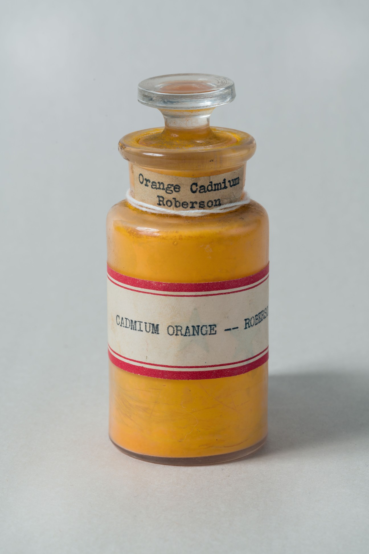 Vintage glass apothecary bottle labeled 'Orange Cadmium' and 'Cadmium Orange – Roberson' with orange pigment inside.