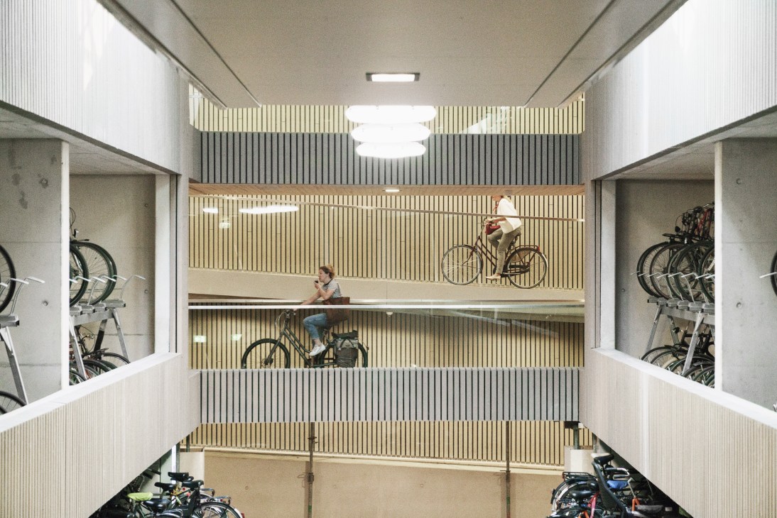 Interior of a modern multi-level bicycle parking garage with organized bike racks and two cyclists using the facility.