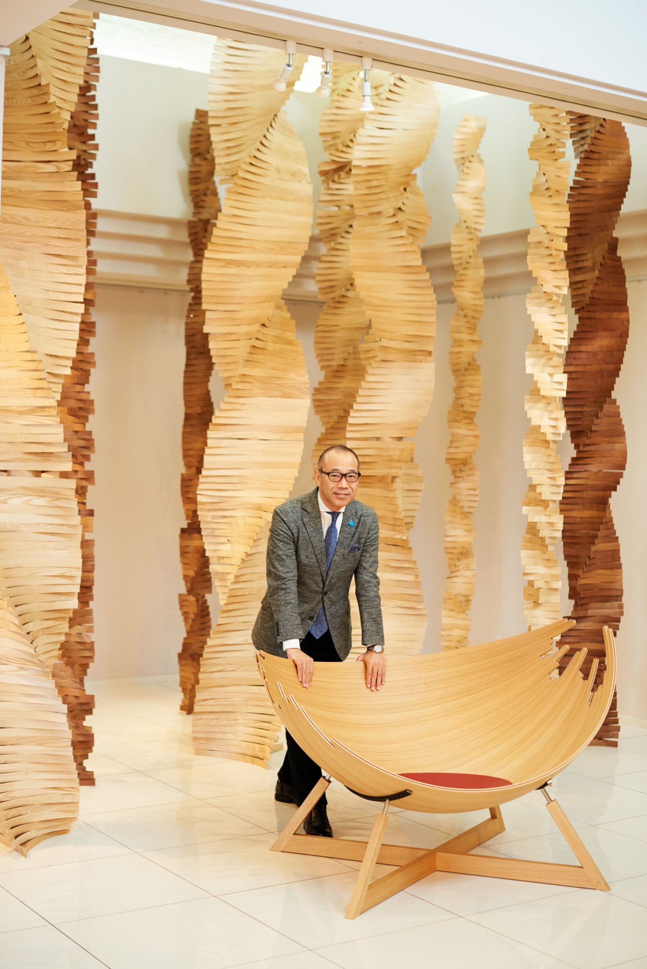 Conde House president Tetsuya Fujita stands beside Jakob Jørgensen's wooden Barca lounge chair in a bright showroom with stacked wood slats.
