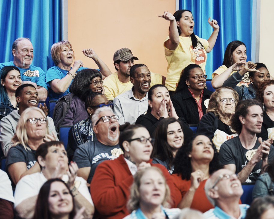 Diverse audience members cheering and celebrating with raised arms during a taping of The Price is Right
