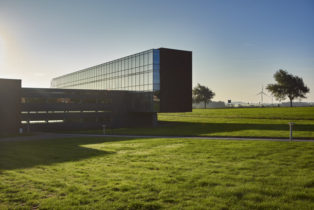 Bang & Olufsen's Farm headquarters with glass and steel upper structure set in green Danish countryside with wind turbine visible.