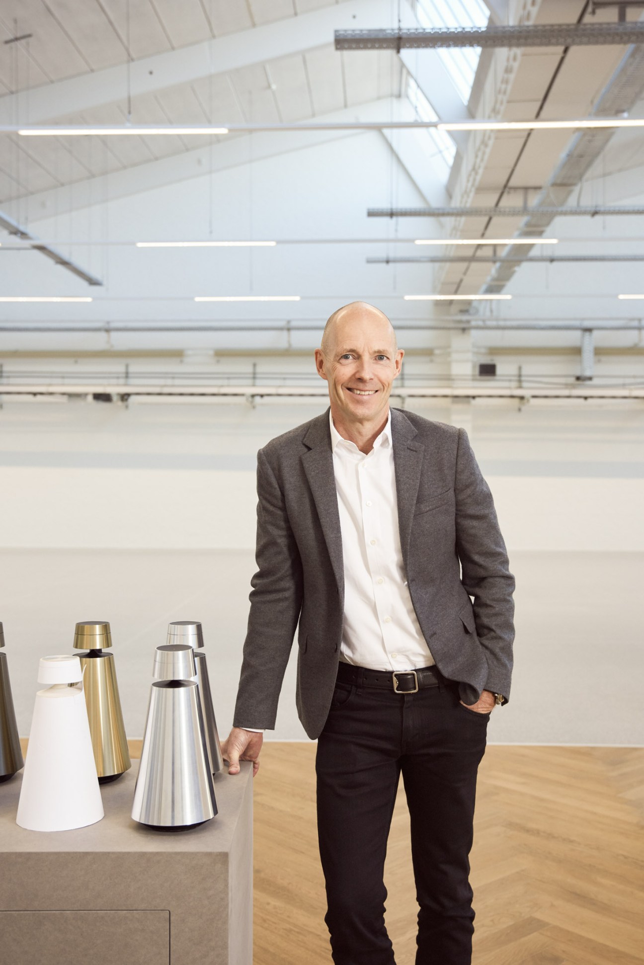 CEO Henrik Clausen standing in a modern industrial space with Bang & Olufsen speaker products on display.