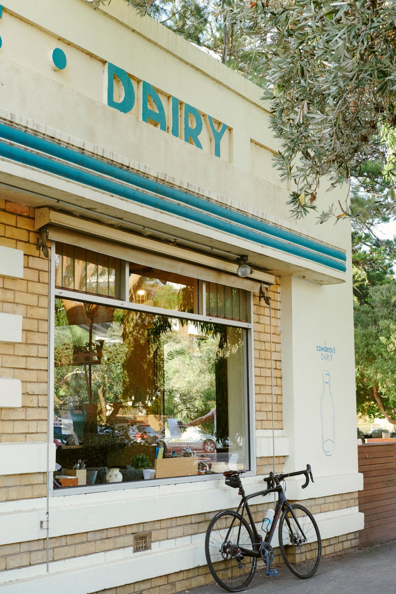 Cowderoy's Dairy storefront with turquoise signage, brick facade, large windows and a bicycle parked outside.