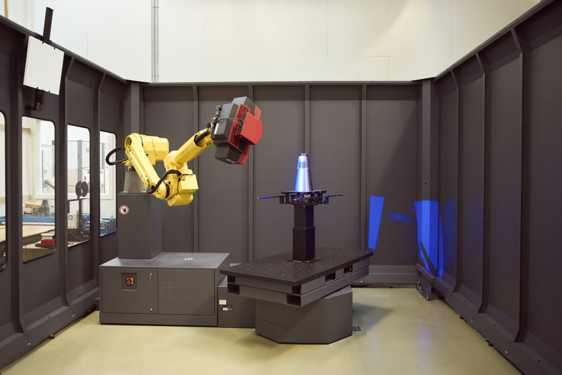 Industrial robotic arm with red gripper in Bang & Olufsen's Innovation Lab testing facility.
