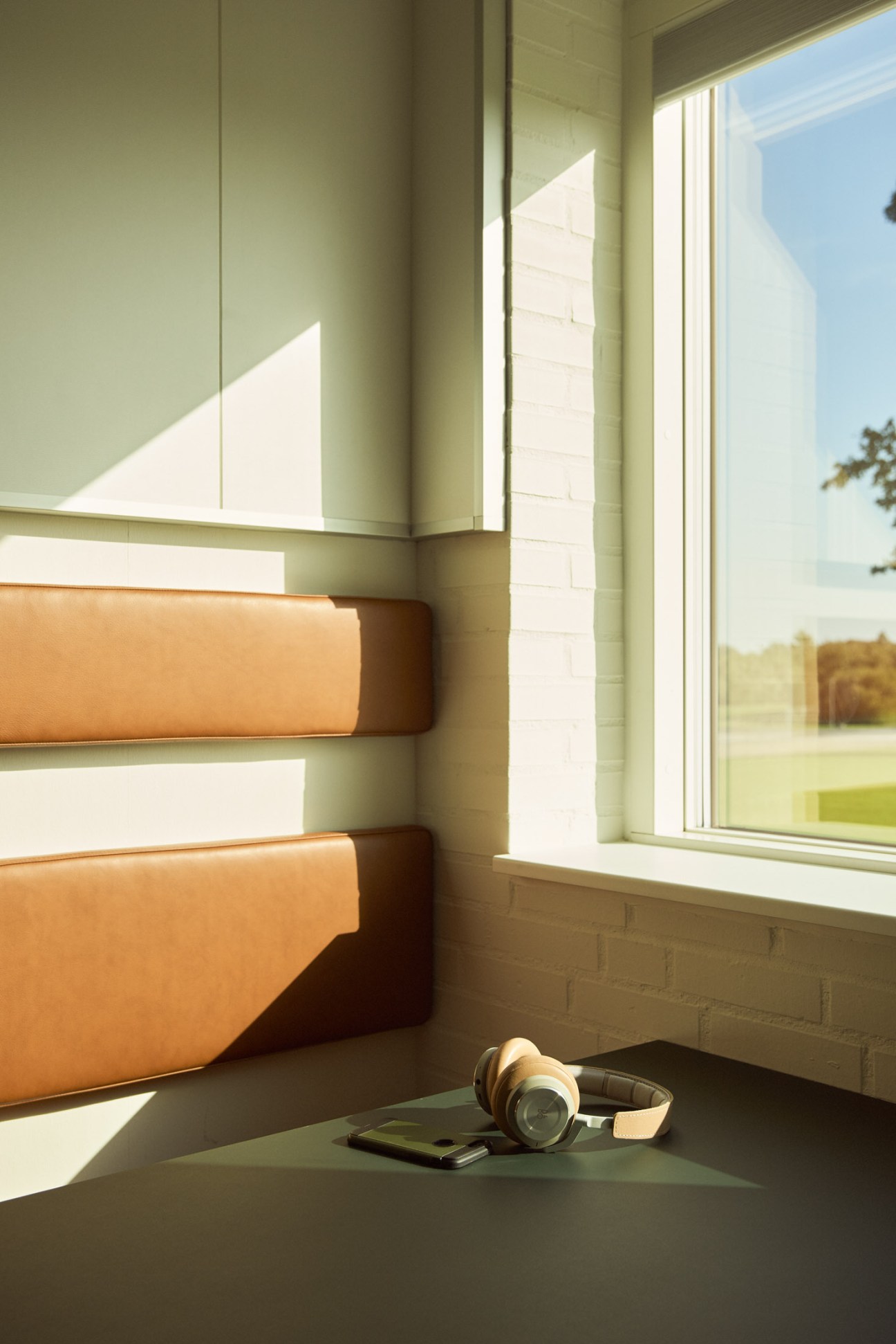 Beoplay headphones displayed on a windowsill with tan leather seating and countryside view.