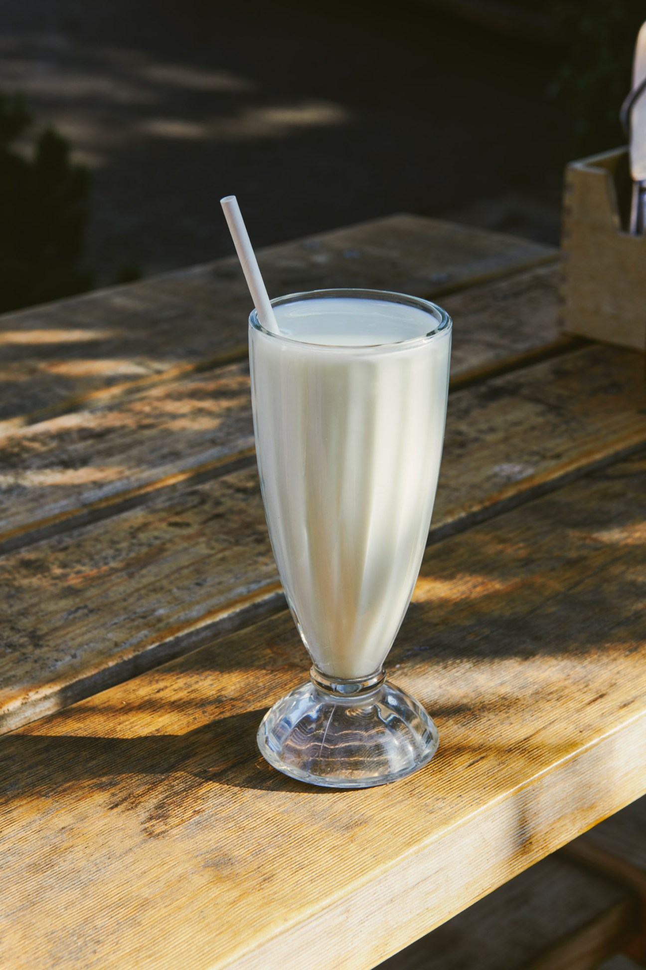 A tall glass of white milkshake with a straw on a wooden table.