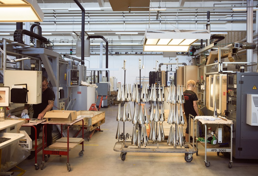 Workers in Bang & Olufsen's aluminium factory with polished metal parts displayed on racks.