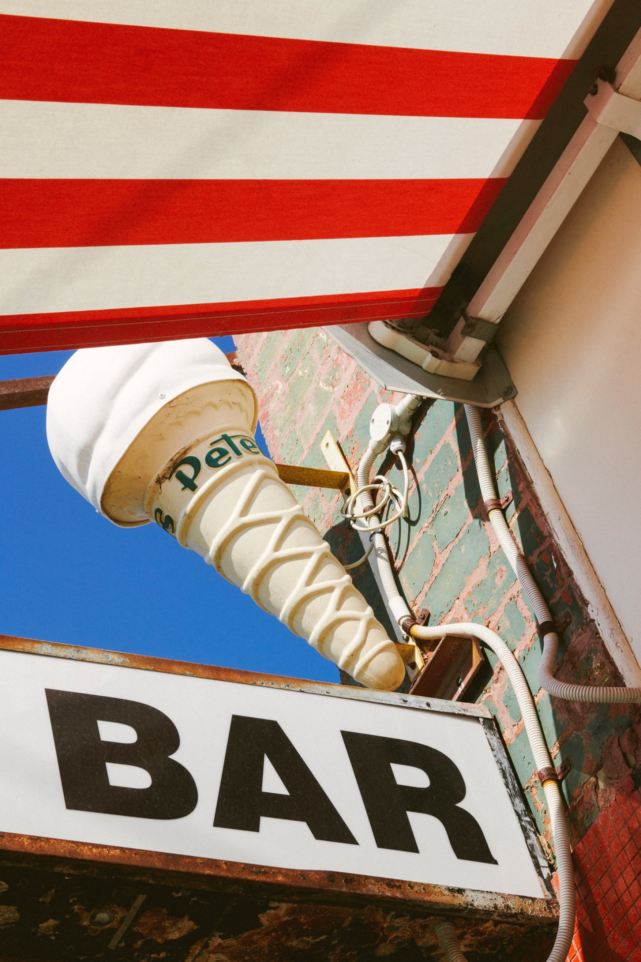 Vintage ice-cream cone-shaped neon light fixture mounted on brick building exterior with red and white striped awning above.