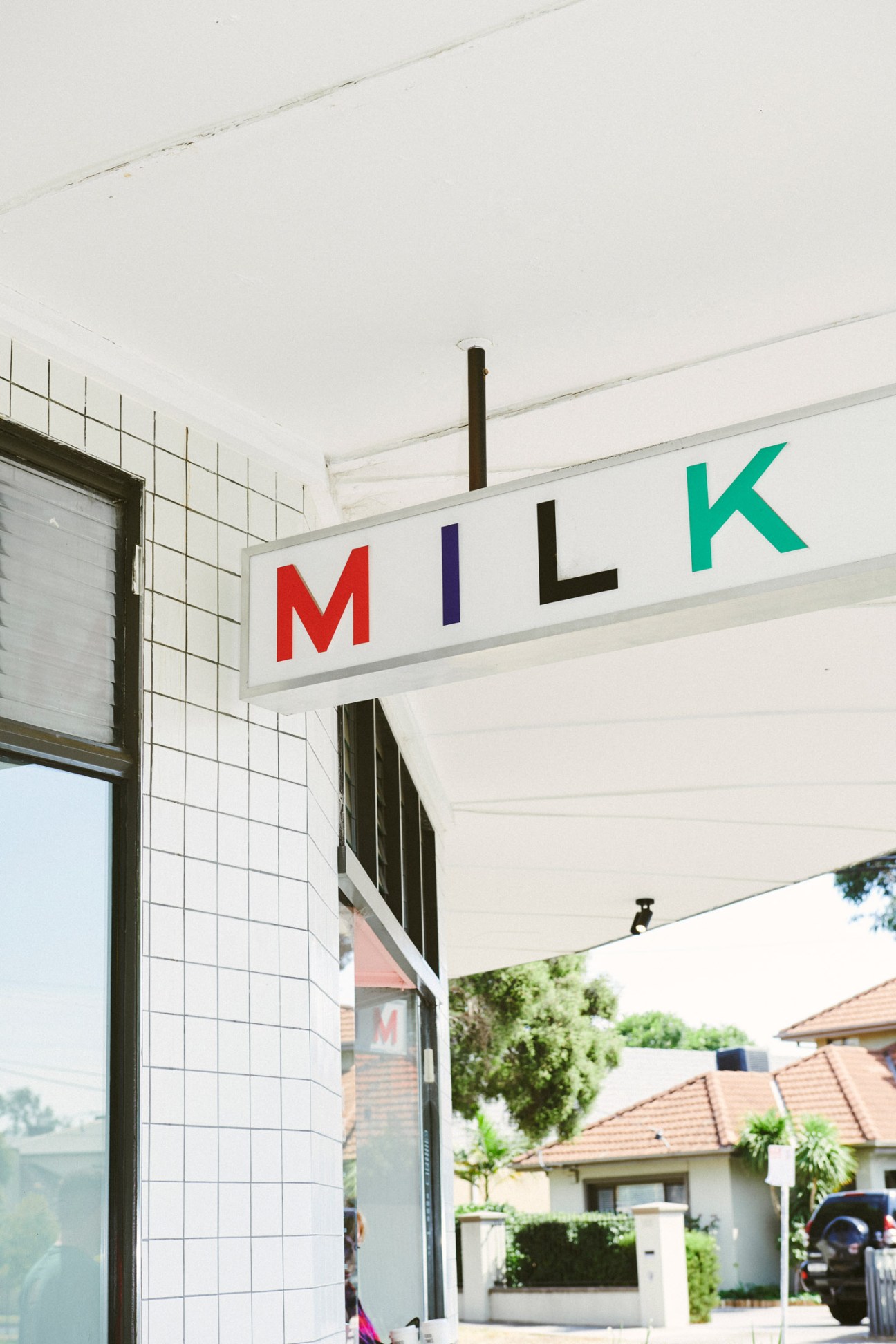 A vintage milk bar storefront with colorful letters spelling 'MILK' on a white facade with tile walls and awning.