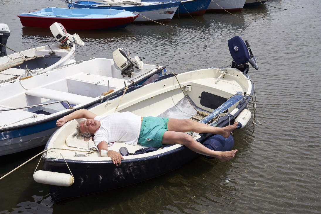 Man relaxing in a small boat among moored fishing vessels in calm water.