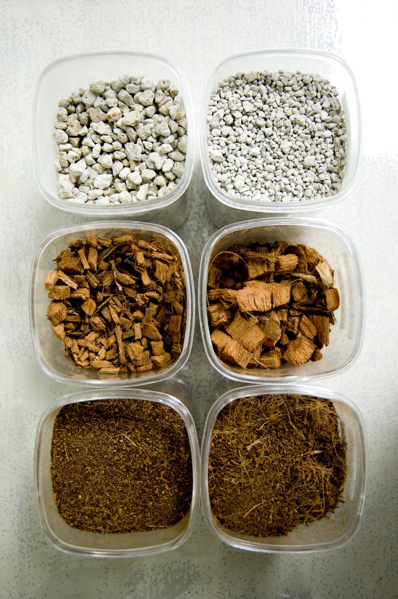 Six clear containers displaying pumice stones, coconut fibre, and soil materials used in vertical garden systems.