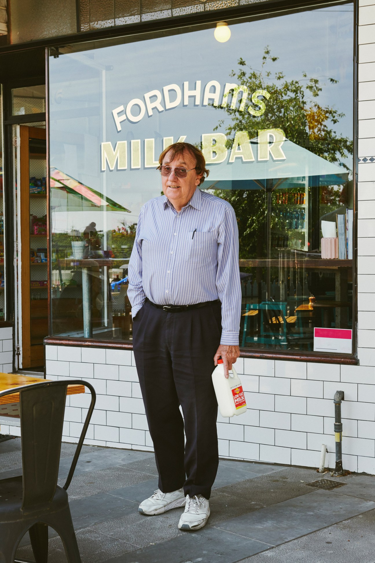 Man in striped shirt standing outside Fordham's Milk Bar holding a milk bottle