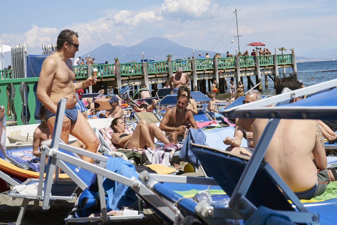 Beachgoers enjoying ice cream on a crowded seaside pier with a green railing and mountain backdrop.