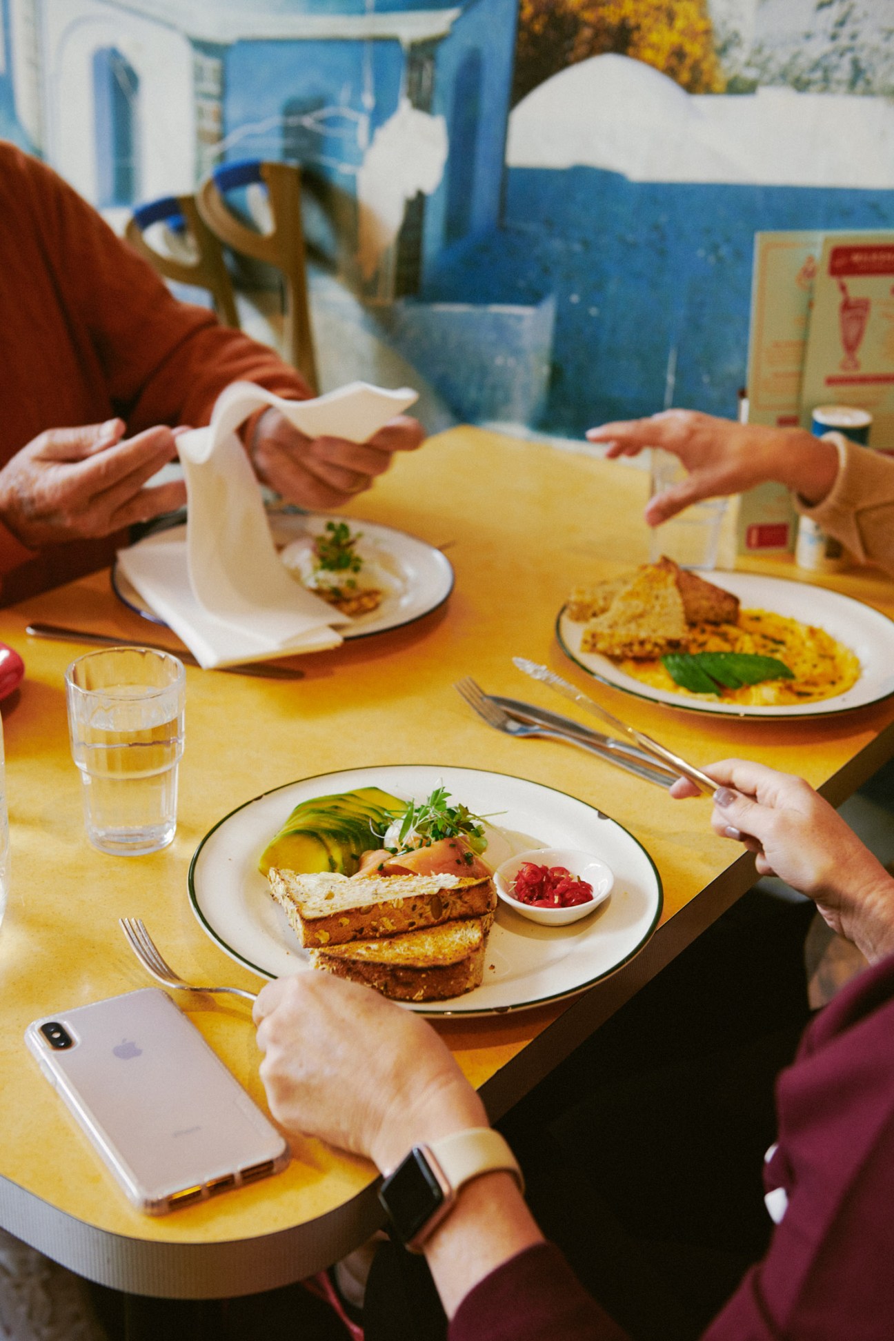 Three people dining at a yellow table with toast, eggs and avocado dishes at Rowena Corner Store.