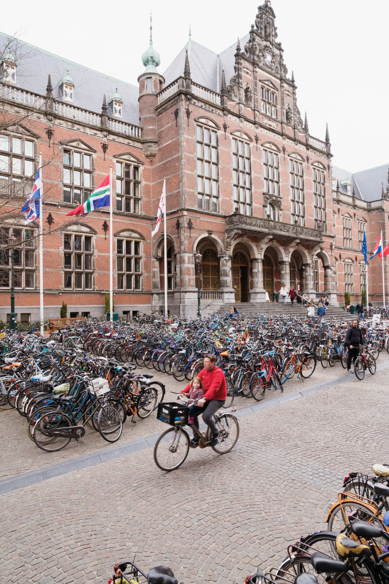 Hundreds of bicycles parked in front of a red brick building with Dutch flags in Groningen.