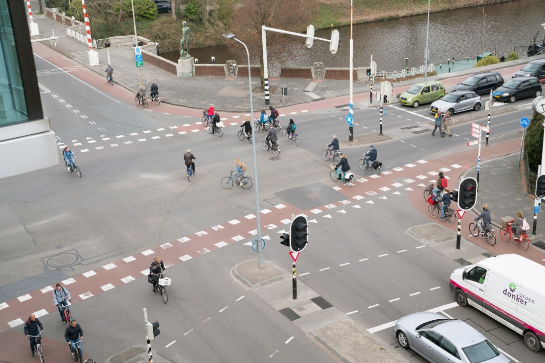 Aerial view of a busy Groningen intersection with multiple cyclists crossing at zebra crossings amid pedestrians and cars.
