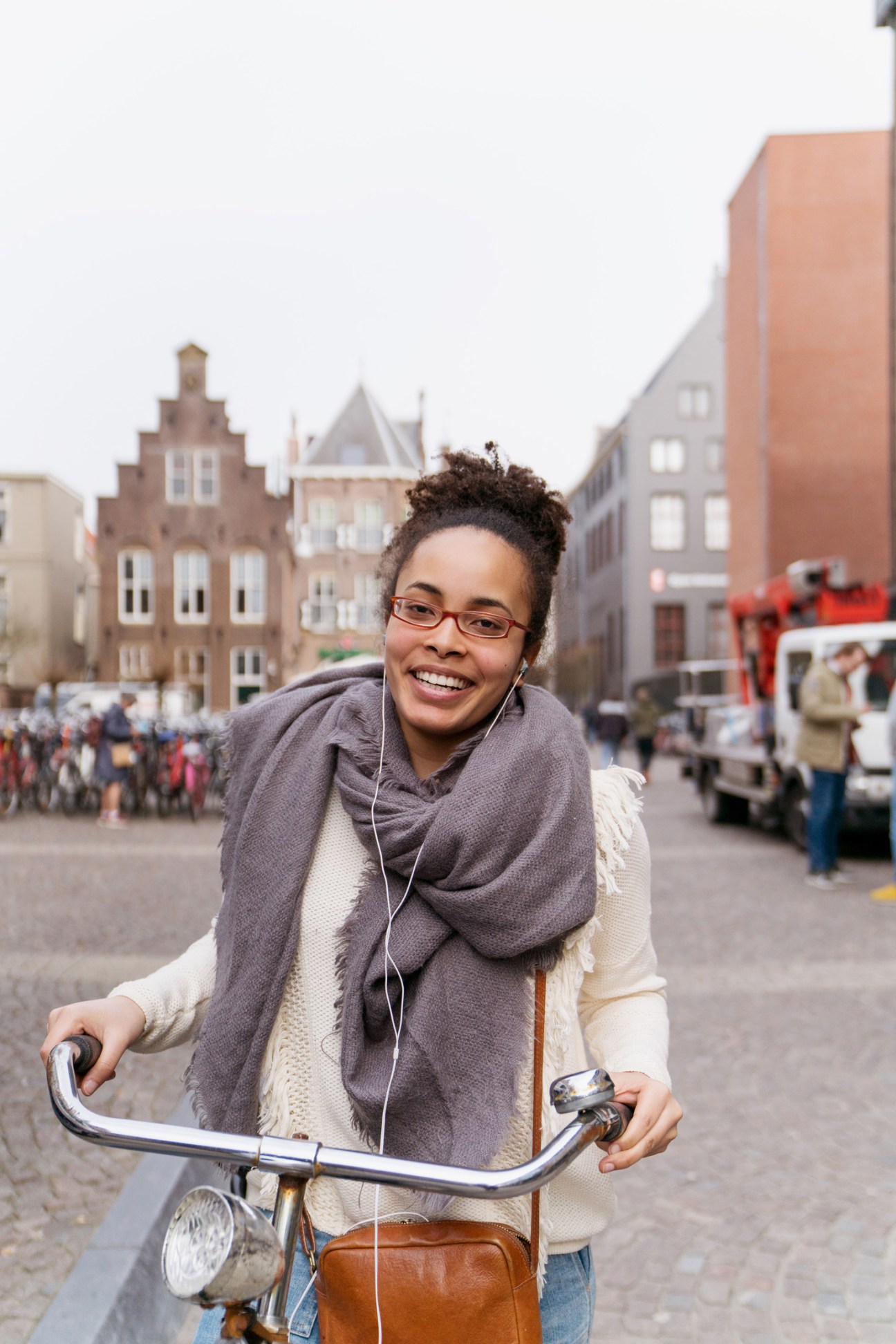 Smiling woman on a bicycle in a European town square with historic buildings and people in the background.