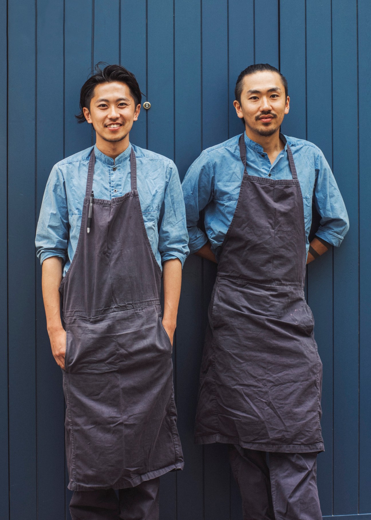 Kabi owners Kentaro Emoto (left) and Shohei Yasuda in matching denim shirts and dark aprons against blue wall