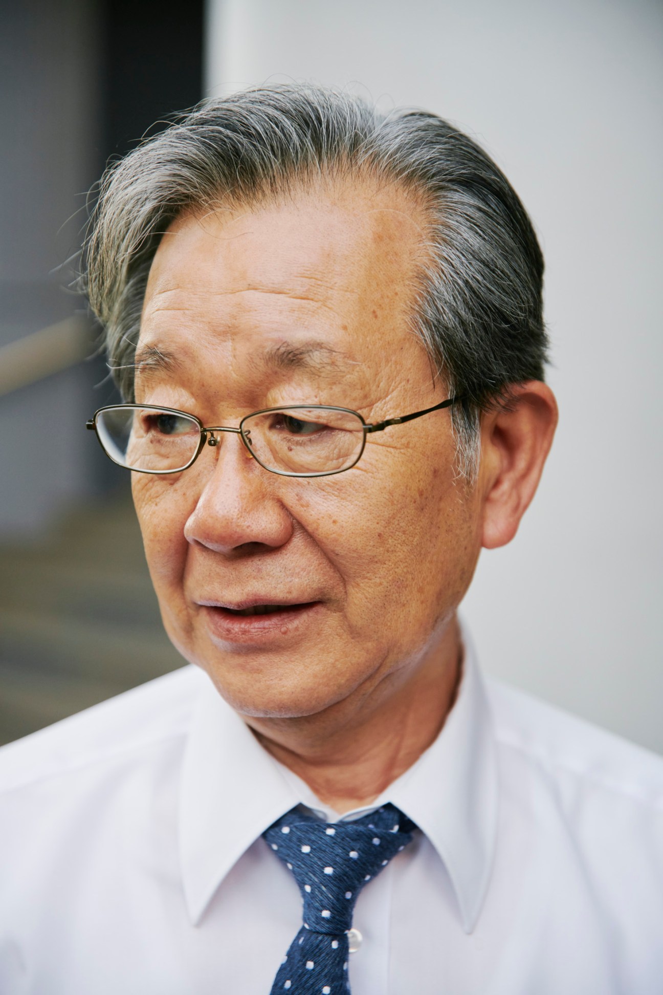 JCP spokesman Toshio Ueki wearing glasses, white shirt and polka dot tie during interview