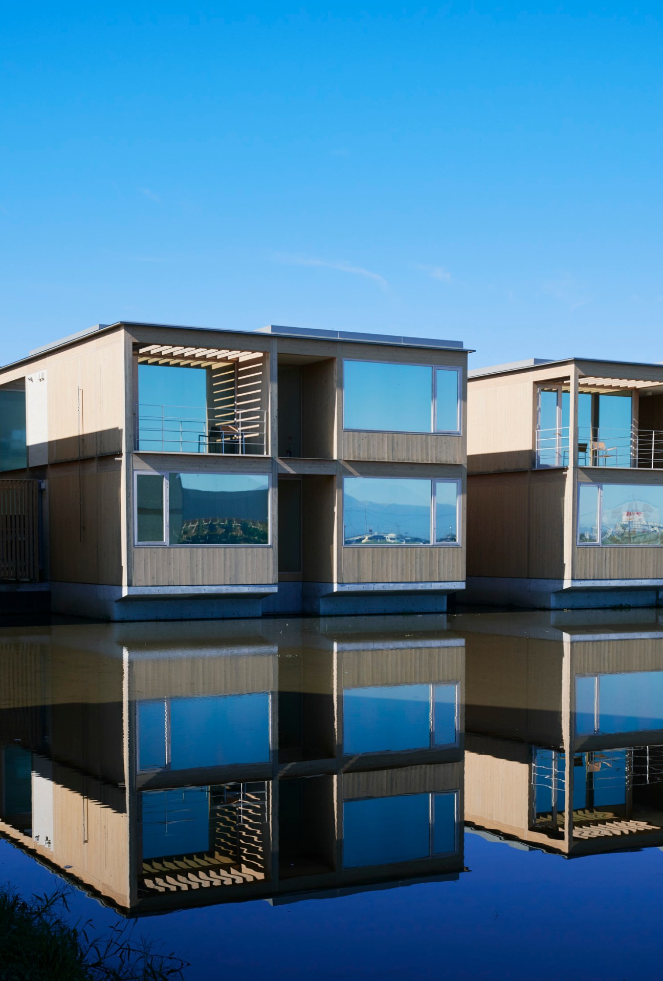 Modern geometric hotel buildings with large windows reflected in still water under clear blue sky