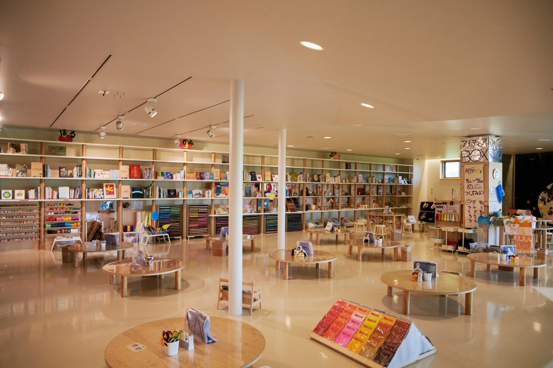Modern library or learning space with wooden tables, bookshelves, and colorful art supplies in bright interior