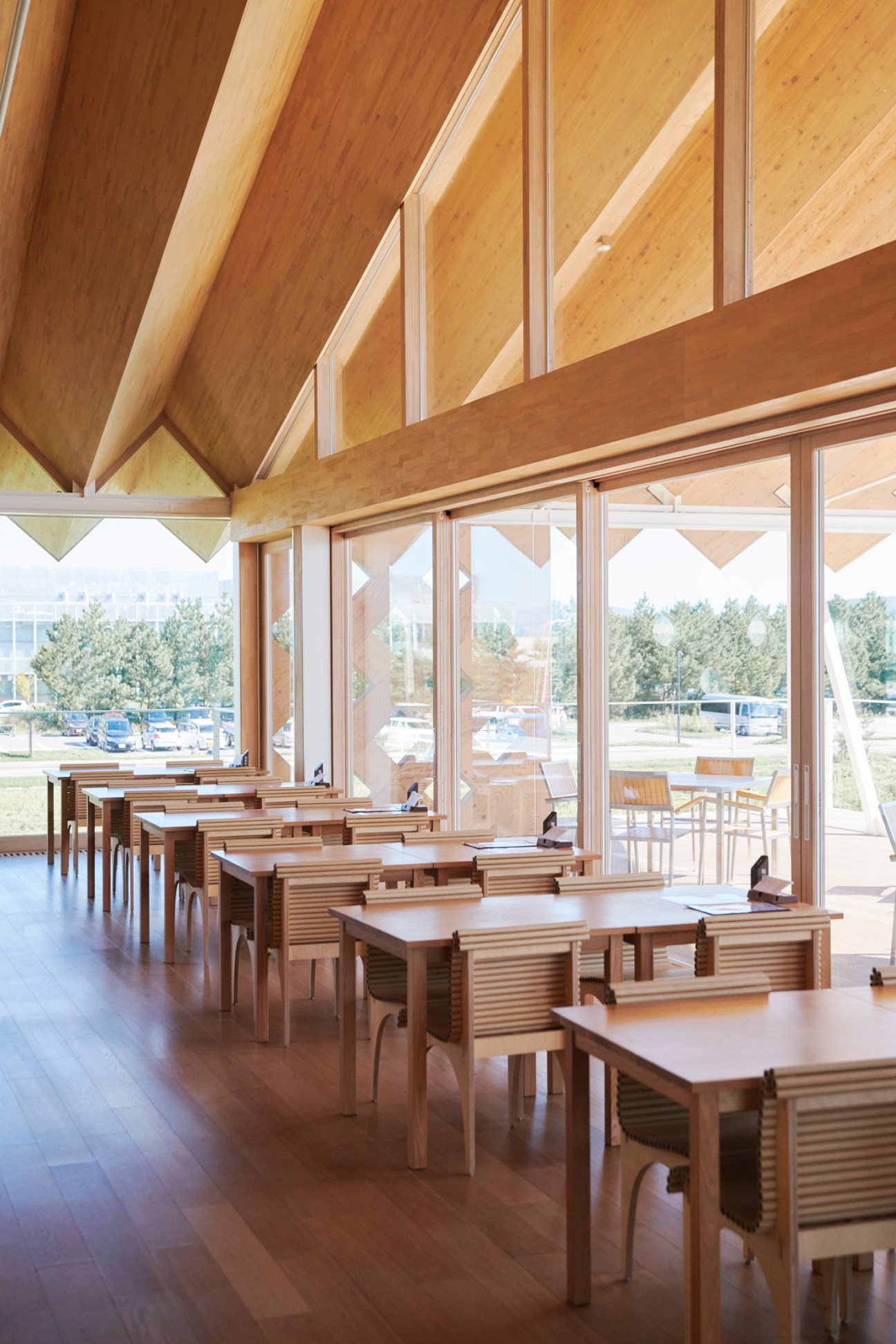 Modern wooden restaurant interior with exposed timber ceiling beams and rows of dining tables near large windows