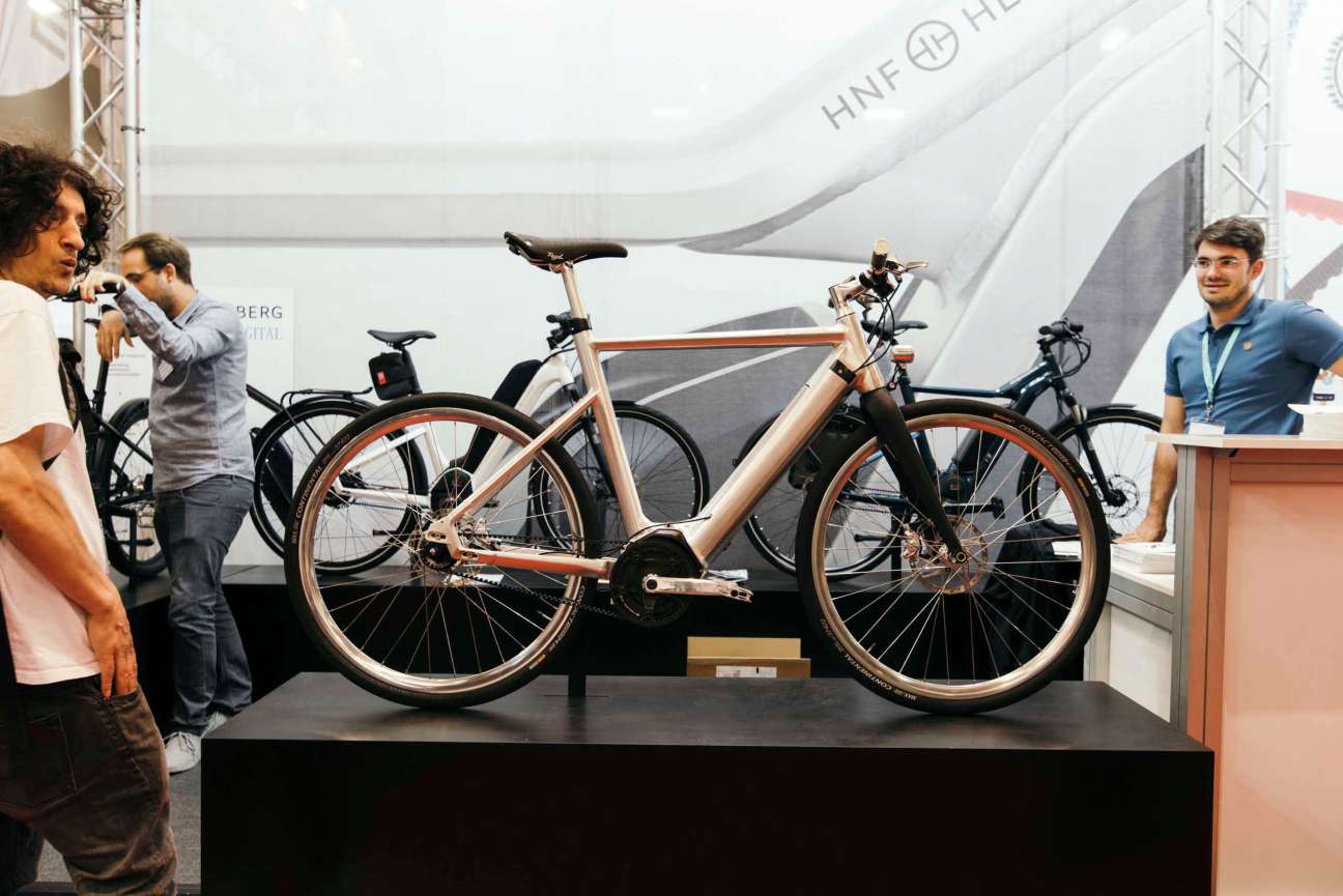 Rose-gold electric bike on display at Eurobike trade fair with attendees nearby.
