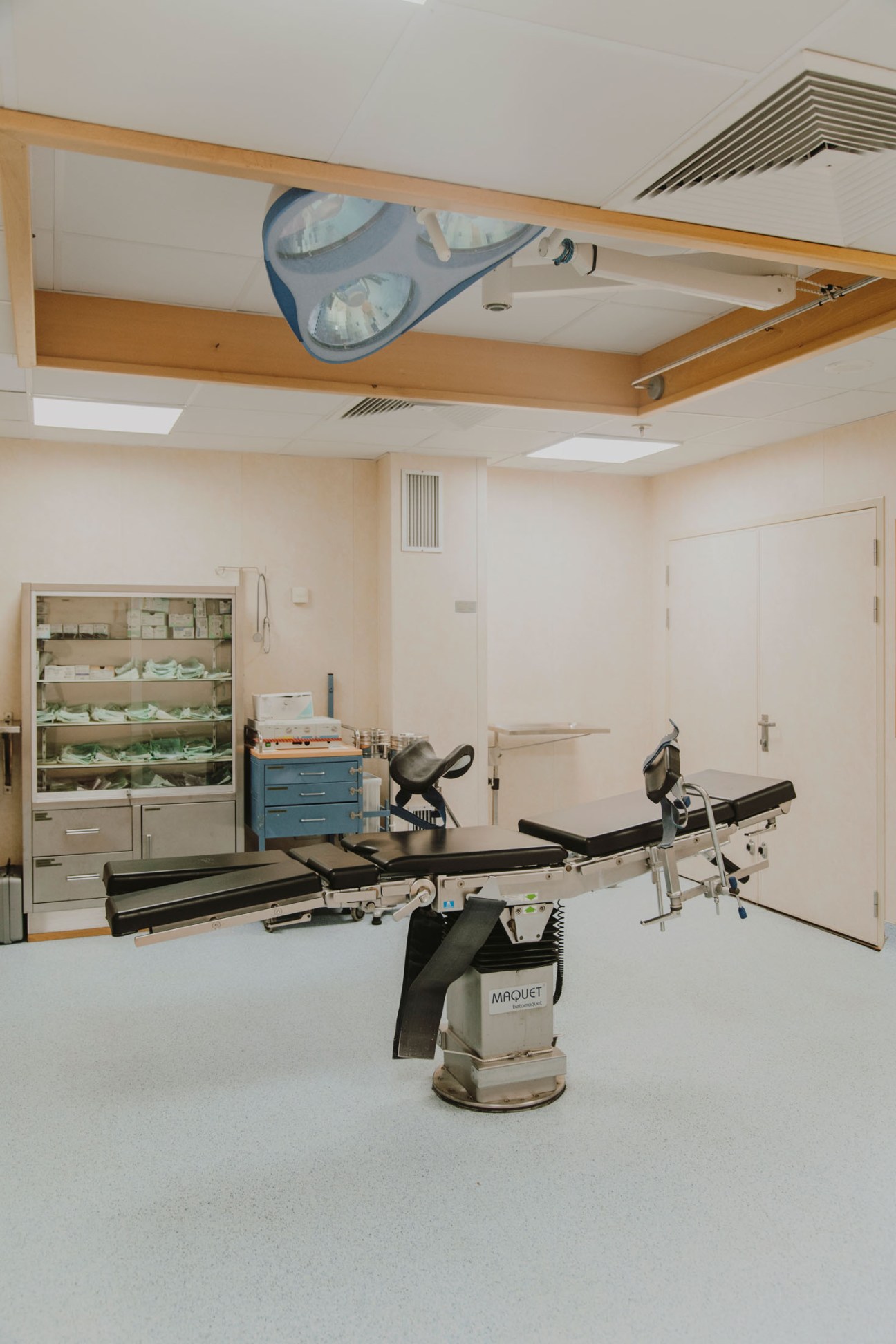 An operating theatre with a surgical table, overhead lighting, and medical equipment and storage cabinets visible in the background.