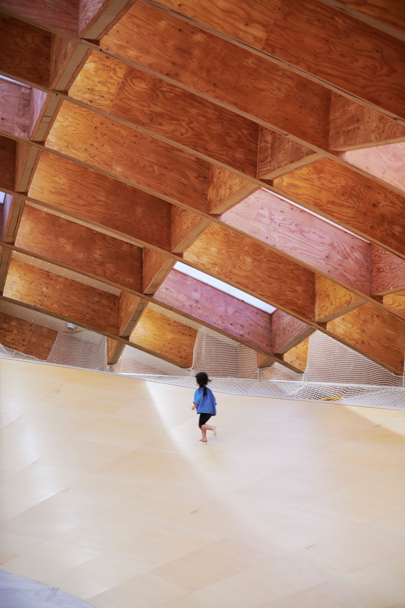 Child running through modern building interior with exposed wooden beam ceiling and mesh safety barriers